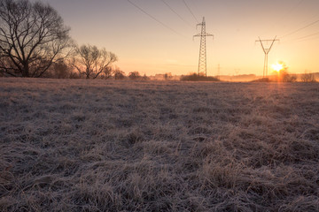 High voltage line supports in fog at frosty spring sunrise morning