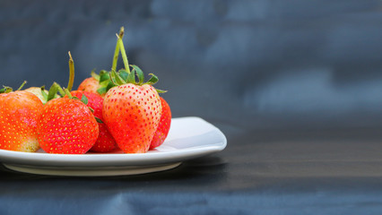 Red strawberry on white plate , black background.
