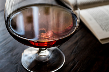 Glass of Cognac with a book on wooden surface.