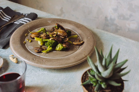 Saut&eacute;ed mushrooms with olive oil, broccoli and pumpkin seeds, on a concrete plate. At the table set