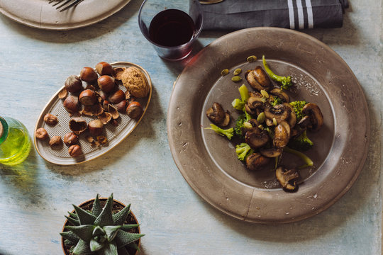 Saut&eacute;ed mushrooms with olive oil, broccoli and pumpkin seeds, on a concrete plate. At the table set