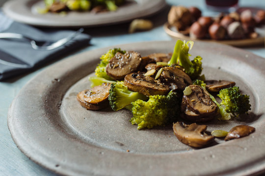 Saut&eacute;ed mushrooms with olive oil, broccoli and pumpkin seeds, on a concrete plate. At the table set