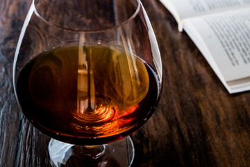 Glass of Cognac with a book on wooden surface.