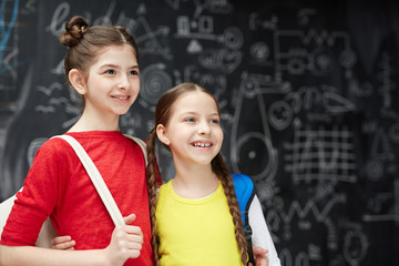 Embracing schoolgirls standing against blackboard