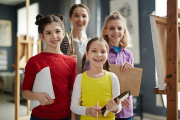 Group of talented kids and their teacher looking at camera in studio of arts