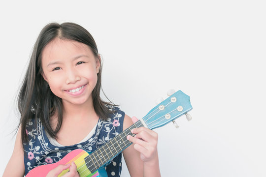 Selective focus beautiful little girl smiling with confidence and playing ukulele on white background. Concept child confidence.