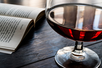 Glass of Cognac with a book on wooden surface.