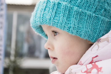A cute little girl in a warm hat close-up, looking away