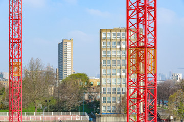 Red building cranes with East London council housing blocks, Robin Hood Gardens, in the background