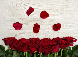 Red roses and petals on a light wooden background, top view