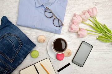 Obraz na płótnie Canvas Planning a trip. Blue shirt, tulips, coffee mug, notebook and phone. Fashionable concept. Top view
