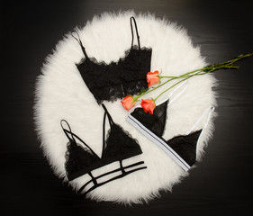 Fashionable concept, three black lace bodices on white fur, orange roses, top view