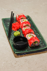 Roll on green plate with ginger, wasabi and soy sauce on creme background