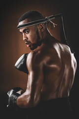 Young shirtless Muay Thai fighter with boxing gloves looking over shoulder, action sport concept