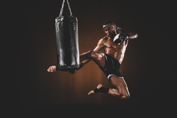 side view of focused muay thai fighter practicing kick on punching bag, action sport concept