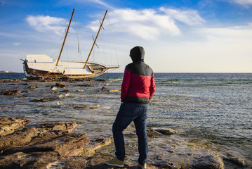 A man look the shipwrecked Boat in Calasetta, on the coast of south Sardinia where is sitting even...