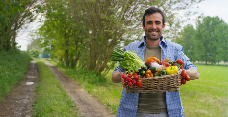 Portrait of a happy young farmer holding fresh vegetables in a basket. On a background of nature...