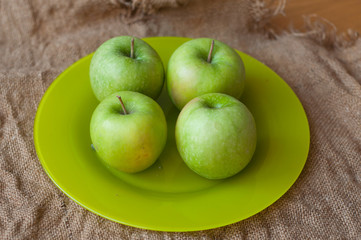 A plate with green apples on the sackcloth texture background