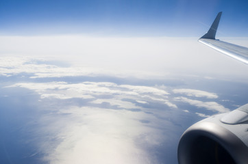 Naklejka na ściany i meble Wing of airplane on clouds and sea