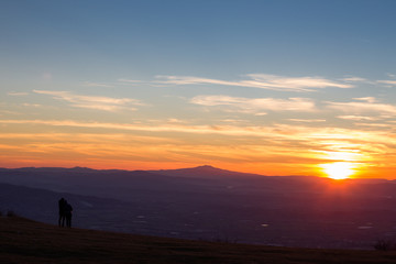 Obraz premium A boy and a girl looking at sunset from the top of a mountain
