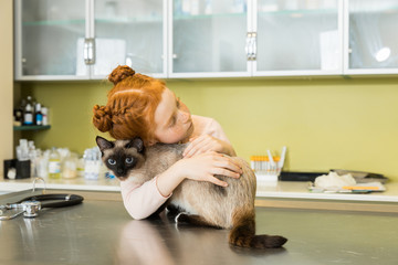 Small red haired girl embrace her cat at veterinary clinic