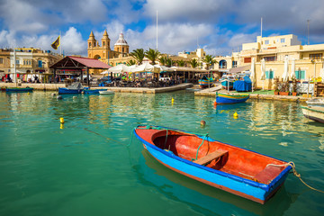 Marsaxlokk, Malta - Traditional colorful maltese Luzzu fisherboat at the old village of Marsaxlokk with turquoise sea water, blue sky and palm trees on a summer day