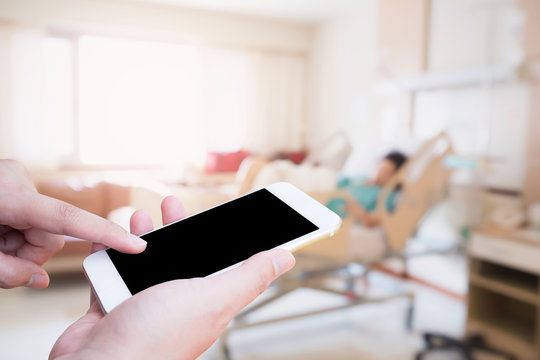 Female hand holding mobile smart phone with blurred hospital room with patient background