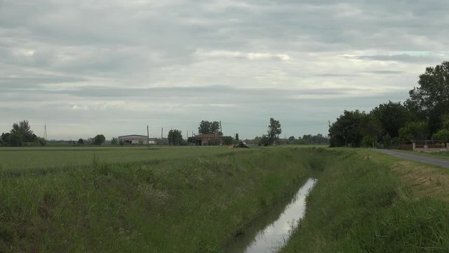 tractor on irrigation channel between asphalted road and agricultural crops