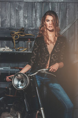 Fototapeta na wymiar Sexy biker in erotic shirt and jeans standing at motorcycle