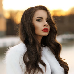 Breast portrait of young beautiful pretty woman with long curly hair and red lips posing outdoors...