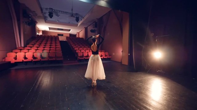 Elegant ballerina dancing in empty theatre. Steadicam. Close-up. Slowmotion.
