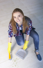  woman sit on floor with  scoop for garbage and smile, looking up. 