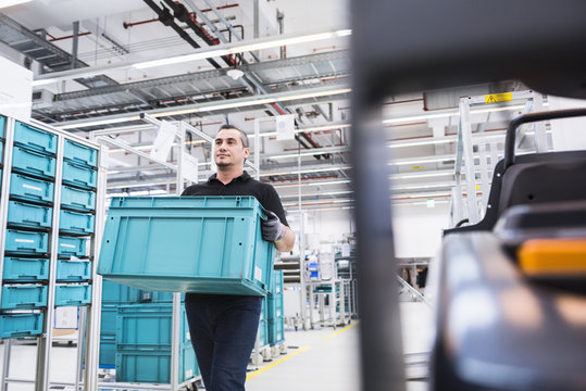 Man carrying box at tugger train in industrial hall
