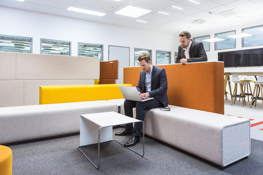 Businessman sitting in conversation pit, colleague watching him