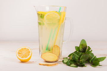 A glass decanter with a summer refreshing lemonade made of lemons and ginger with mint added on a white wooden background. Detox water. Ingredients. Cleaning the body of toxins, vitamins