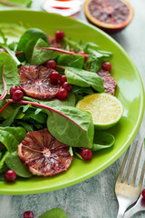 Fresh spring salad with arugula, beet leaves, avocado, red orange slices and cranberry on wooden table. Selective focus