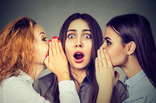 Three young women telling whispering a secret gossip each other in the ear