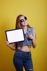 Sunglasses ginger girl hides for white painting on yellow background