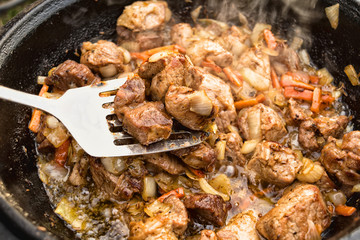 Meat with carrots and onion in cauldron on fire