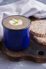 Creamy mushroom soup puree in a blue mug with crisps on wooden board. Healthy dinner. Vegetarian food. Clen and healthy eating concept.