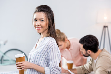 portrait of smiling businesswoman holding coffee cup with colleagues near by