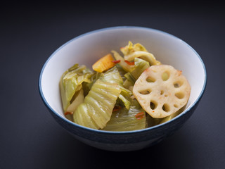 Korean kim chi made from fermented vegetables such as cabbage, carrots and lotus root, in small asian bowl isolated on black background