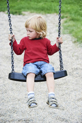 Adorable toddler blond boy having fun chain swing on outdoor playground.