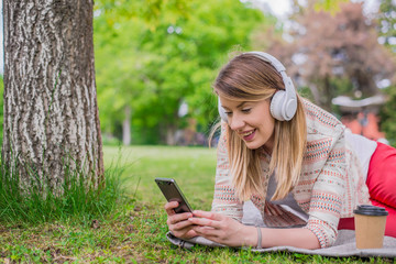 Fototapeta na wymiar Relaxed woman listening to the music with headphones lying on the grass
