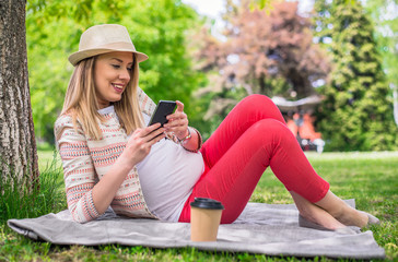 Portrait of young happy woman lying on grass holding cell phone and coffee to go. Full body portrait of happy woman lying in grass texting with smart phone
