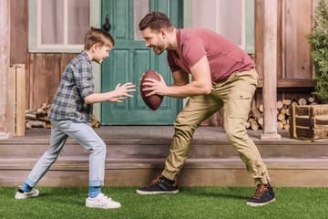 father with little son playing american football with ball at backyard, dad and son playing