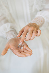 A gentle bride in a lace wedding dress holds earrings with pearls on her palm and touches them with her hand. Bride's morning