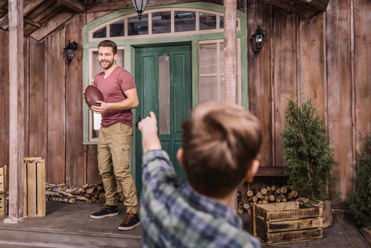 Father With Little Son Playing American Football With Ball At Backyard, Dad And Son Playing