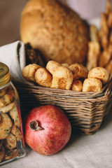 A wicker basket with bread, a glass jar with biscuits and a pomegranate on a linen table