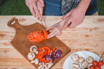 Close-up partial view of father and son cutting fresh vegetables on wooden cutting board, dad and son cooking concept